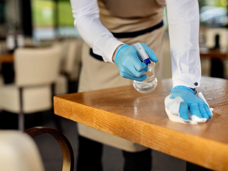 Close-up of waiter disinfecting cafe tables after work. Close-up of waiter spraying cafe tables with disinfectant due to coronavirus epidemic.